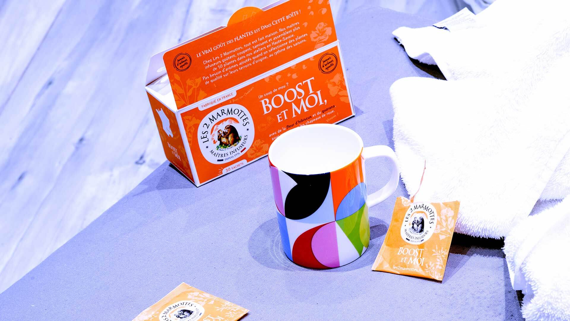 Boîte de Boost & Moi posé sur une table à côté d'une tasse et d'une serviette de sport