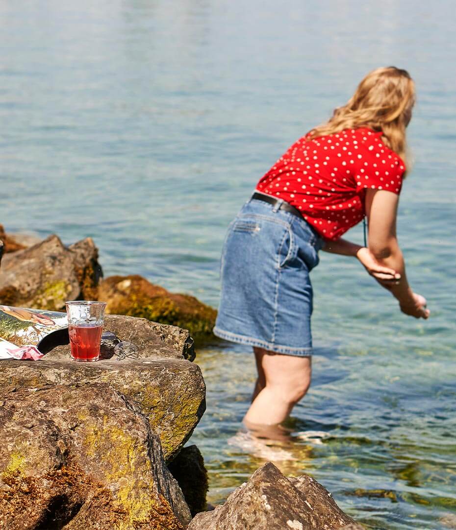 Femme baignant ses jambes avec un verre d'infusions froides sur un rocher
